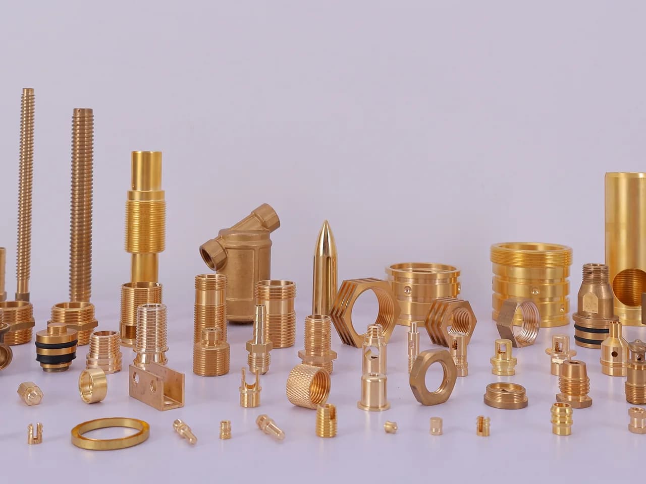 The full range of turned brass parts — threaded studs, hex nipples, bushes, nozzles and pins laid out on the studio table